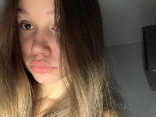 MisaQueen a de longs cheveux bruns avec des pointes blondes, des lèvres roses et pulpeuses, et des yeux marrons sur une photo de profil. Son nez est légèrement retroussé, et son expression est neutre..