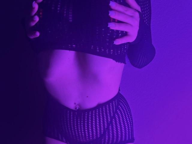 BalletSwan's flat stomach with a navel piercing, wearing black fishnet lingerie, hands on her chest, purple-lit, showing her small tits and lower belly.