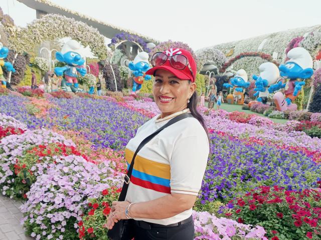 MelissaDelici met een rode muts, een wit shirt met een gele-blauwe-rode streep, zwarte braces, lachend, roze bloemen, blauwe cartoon-beelden, een zwarte tas vasthoudend, paars haar, zonnebril op de muts..