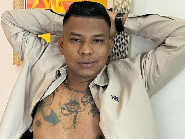 SamSexy69, senza camicia, giacca beige, tatuaggi sul petto, capelli neri, braccia dietro la testa, orologio al polso, collana, leggero sorriso, pelle marrone media, guarda la fotocamera, casual, sicuro di sé, sexy..
