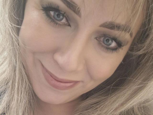 CandyLadyZ has blue eyes, full lips with pinkish lipstick, and blonde hair with bangs. She's smiling, showing off her eyelash-heavy eyes and slightly raised eyebrows.