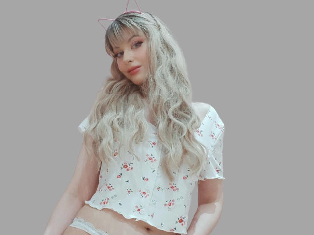 ChloeKiss-hot with long wavy blonde hair, pink cat ears, white floral top, and white lace panties, showing a hint of her ass. Soft makeup, cute, confident.