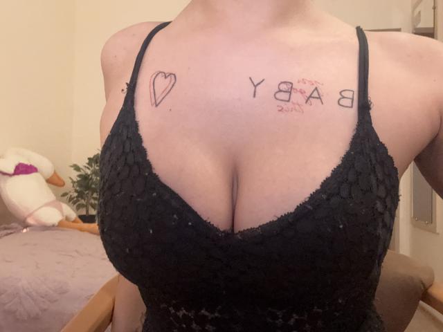 El vestido de encaje negro de Kametia, que muestra sus grandes senos con un tatuaje de corazón en el lado izquierdo y un tatuaje que dice "YEA 8" en el lado derecho, en una habitación con poca luz..