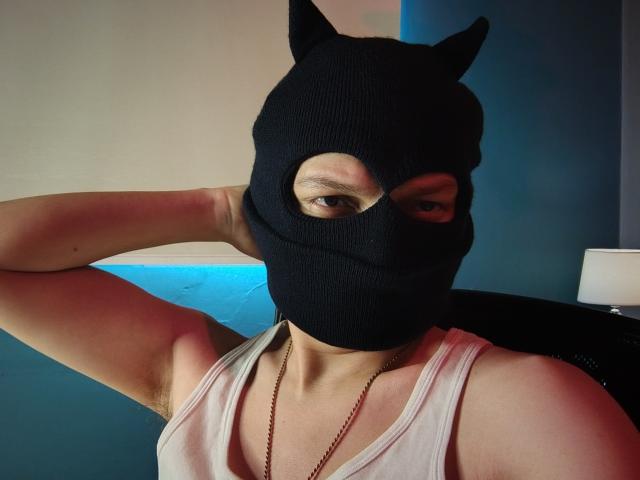 ErossGuy wearing a black knuckle mask with cat ears, white tank top, and a necklace, raising one arm. Visible armpit, brown eyes, and slight smile.