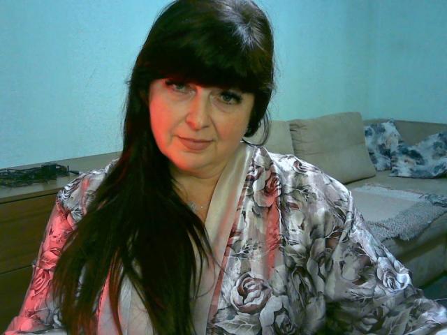BiancaLady with long black hair, wearing a floral silk robe, sitting, has pale skin, red light on left side of face, looking slightly to the right, subtle smile.