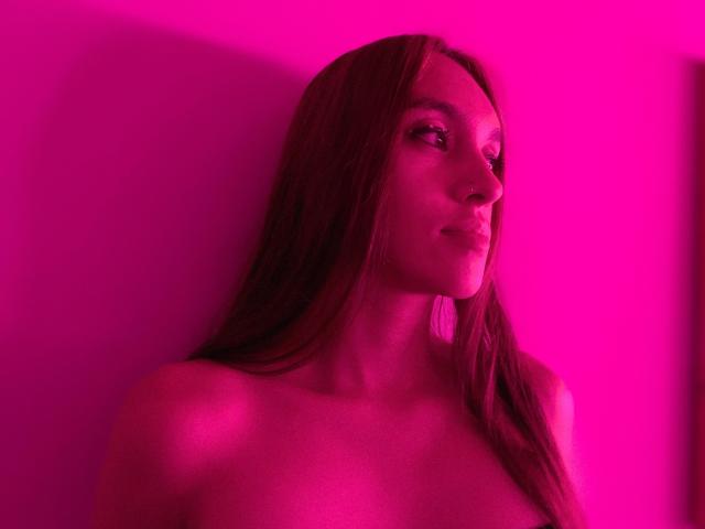 SofySweety with long brown hair, topless, pink neon lighting, side profile, soft smile, visible nose ring, subtle makeup, gentle shadows, pink light highlighting her smooth skin.