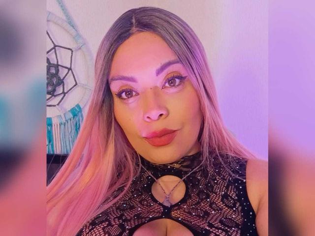 VictoriaRoyale with pink ombre hair, full red lips, and dark eyeliner, wearing a black mesh top with a cutout, looking at the camera with a confident expression.