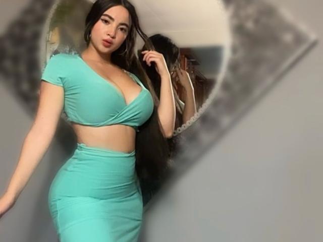 Alisonn Walkerr indossa una canottiera corta verde acqua aderente e una gonna a vita alta abbinata, mettendo in mostra il suo seno prosperoso e i suoi fianchi formosi, con lunghi capelli scuri e un riflesso nello specchio..