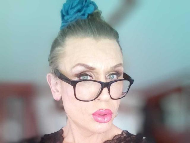 LilianaShe with blonde hair in a blue scrunchie, black glasses, pink lipstick, and a pouty face, showing off her blue eyes and slightly raised eyebrows.