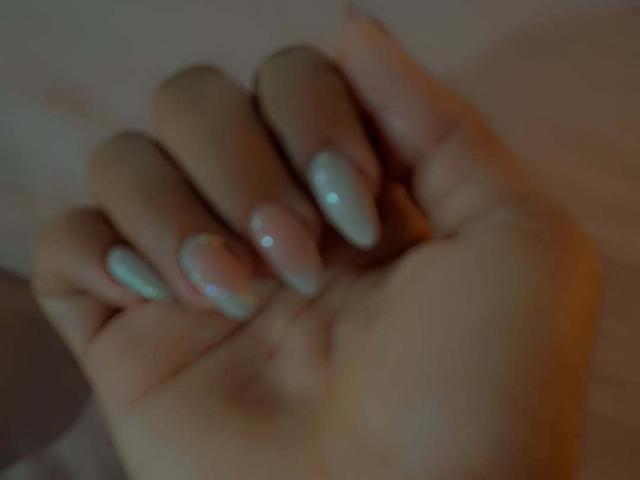 JackelineRoset's hand with long, shiny, pastel-colored nails (pink and blue) is centered in the image. Her skin is light and the focus is on her fingers.