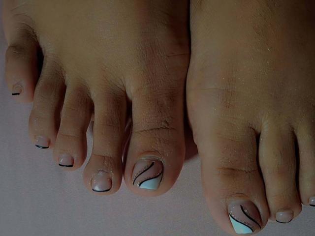 JackelineRoset's feet with a dark brown skin tone, showing her painted toes featuring a light blue and black striped design on a glossy, nude polish base.