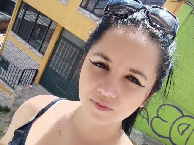 Kkatalina has black eyeliner, dark hair, and sunglasses on her head. She's wearing a black top, showing her small, round ass. Her skin is light and she's smiling.
