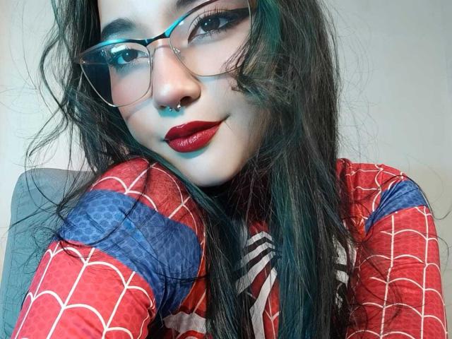 LyRose with long black hair, glasses, red lipstick, nose ring, and red spiderman shirt, smiling slightly, looking at camera. She's got a cute, sexy, nerdy look.