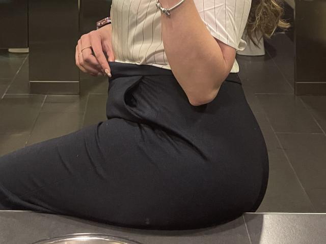 JennyLawry's butt in tight black pants, white pinstripe shirt, bracelet on wrist, pulling down waistband, visible ring on hand, sitting on dark tile floor, partial reflection.