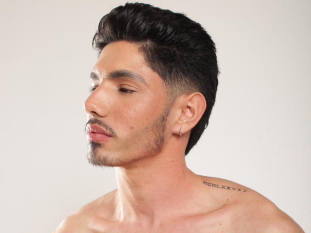 FabrizzioHot with short, dark, styled hair, light skin, small earrings, and a tattoo on his neck. Shirtless, showing a clean-shaven face and a small mustache.