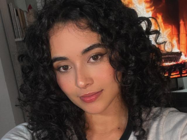 VivienneLaurent has curly black hair, brown eyes, and pink lips, wearing a white shirt. She's smiling softly with a slight tan and a cute nose.