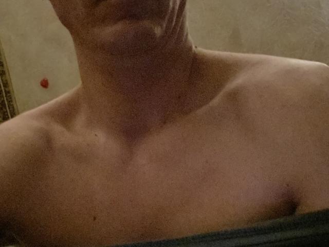 La poitrine nue de Jimmy Clark, légèrement musclée, avec une clavicule visible et une serviette verte recouvrant sa partie inférieure. Son cou est légèrement incliné. L'image est faiblement éclairée..