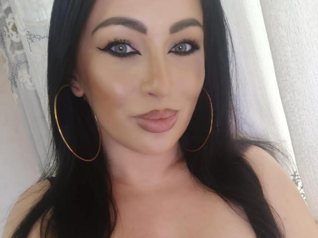 KimStar with black hair, green eyes, and gold hoop earrings, has pouty pink lips, thick black eyeliner, and a smooth, tan complexion. Her tits are not visible.