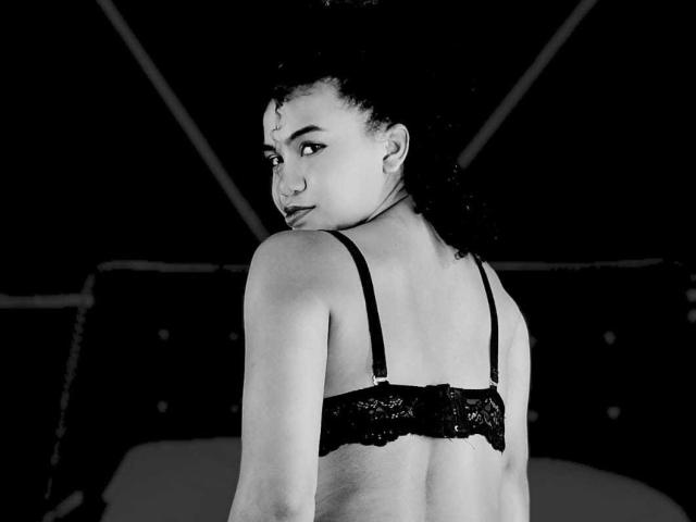 Black-and-white photo of LizzyClasteton with curly hair, looking over her shoulder, wearing a lace bra, showing her bare back and small, cute ass. Her face is slightly turned.