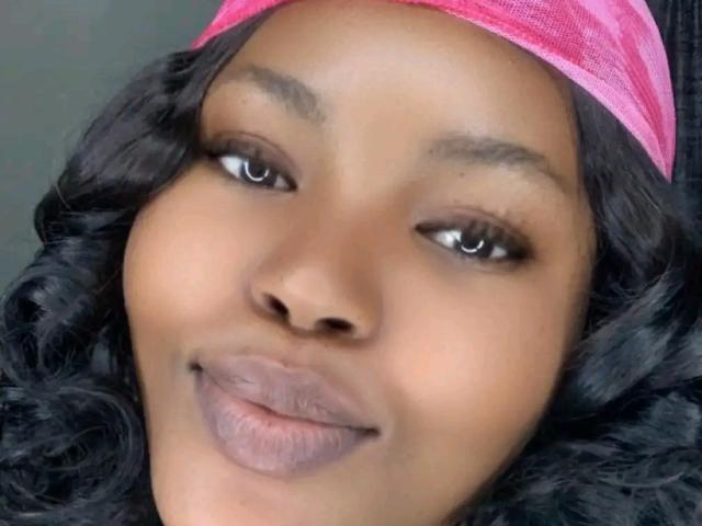 Morenari's face with dark brown skin, curly black hair, pink headscarf, full lips, and brown eyes, smiling slightly. Boobs not visible, ass not visible, tits not visible, pussy not visible.