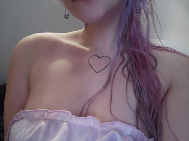 A WhiteKrol tem uma tatuagem de coração no peito, cabelo rosa e roxo molhado, e uma blusa rosa sem alças, que mostra seus ombros nus e seios pequenos..