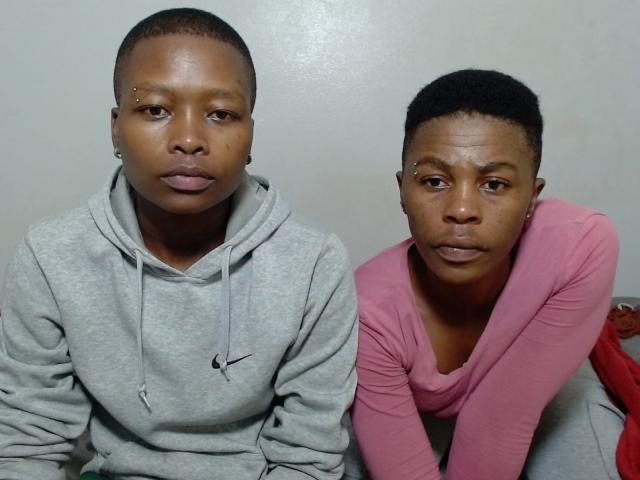 Sexyboobaex5 in gray hoodie and sexyboobaex5 in pink long-sleeve top, both with short black hair, serious expressions, sitting closely together. Sexyboobaex5 on left, sexyboobaex5 on right.