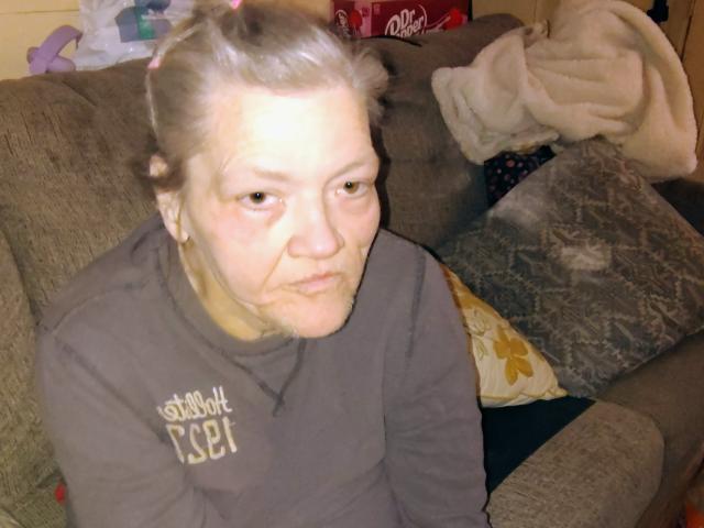 Almethicaandalmetha has pale skin, grayish-brown hair in a messy bun, and a slightly annoyed expression. She's wearing a brown shirt with "Southern" text. She's sitting on a couch.