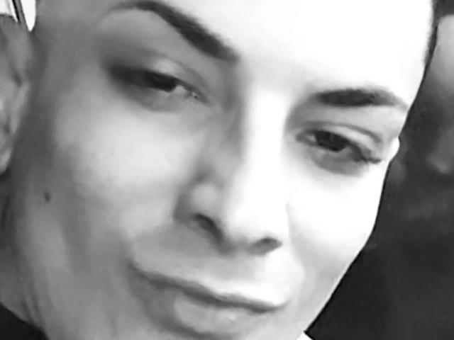 HispanoX's face is in a black and white selfie, showing a slight smirk with half-closed eyes and a small mole on the left cheek. His eyebrows are thick and dark.