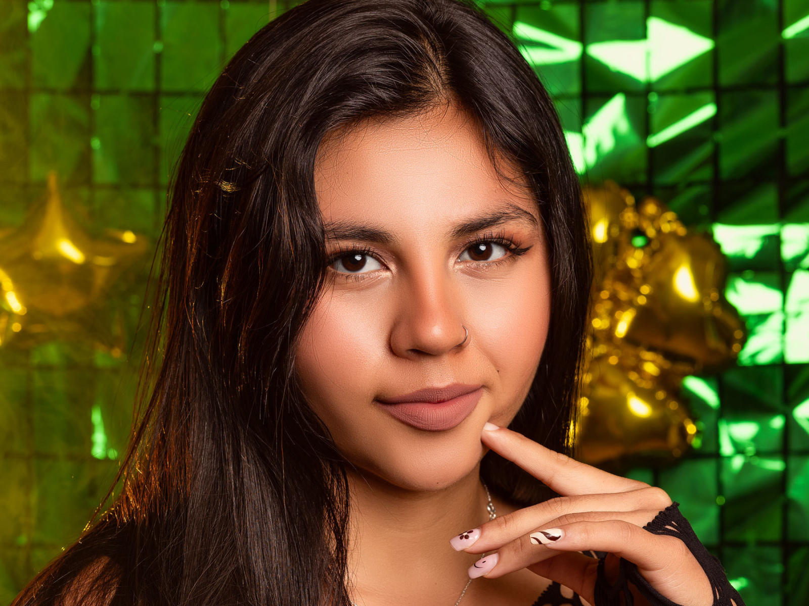AmyXSimpson has long black hair, brown eyes, and a slight smile. She's touching her chin with a finger, showing off her manicured nails with pink and black designs.