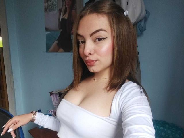 CloeWills has brown hair, white eyeliner, and is wearing a white top that shows her tits. She's smiling with a nose ring and a gold necklace.