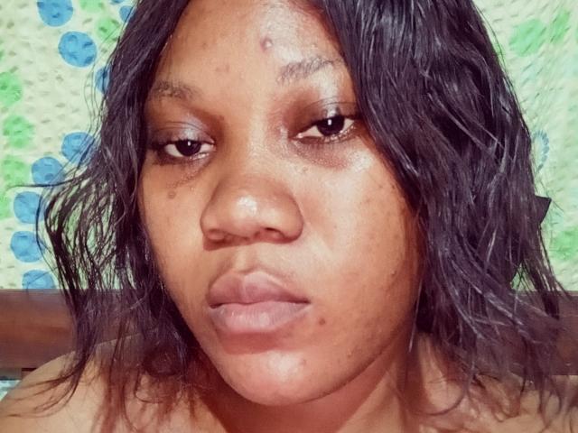 Davlov's face, dark brown skin, wavy black hair, small acne spots, brown eyes, slight pout, bare shoulders, green and blue patterned background.