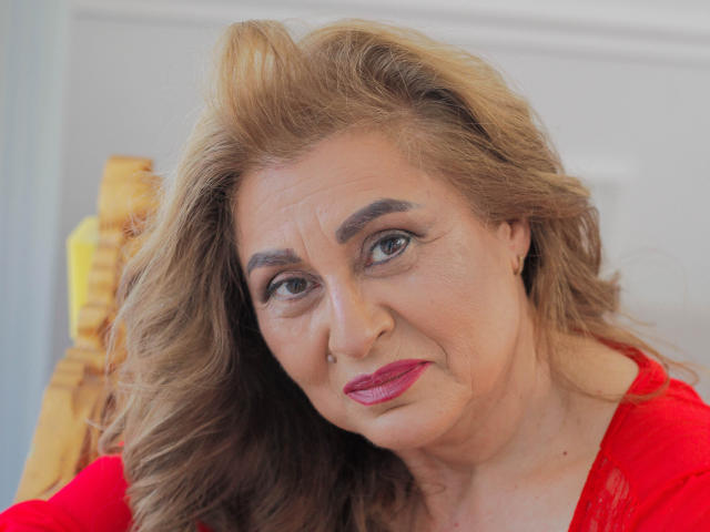 KarlaHartley has light brown wavy hair, red lipstick, and a nose piercing. She wears a red lace top, looking slightly annoyed with raised eyebrows. She's a middle-aged woman.
