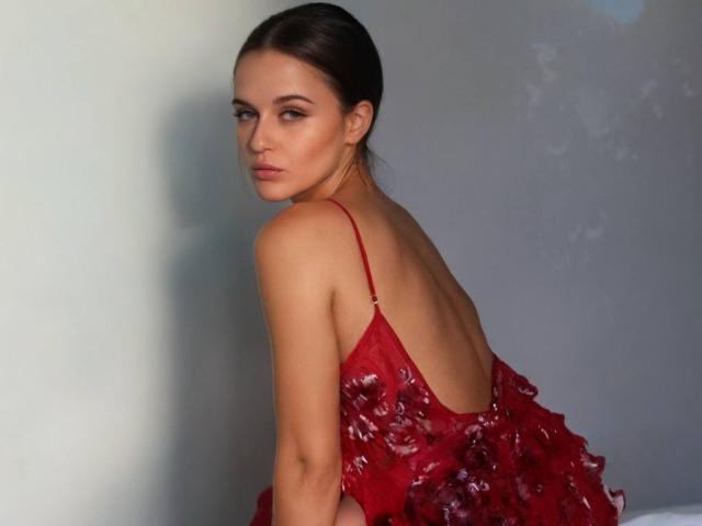 MaribelRiverr with red, ruffled dress, backless, showing her ass, brown hair in a slick bun, looking over her shoulder, serious expression, fair skin, studio light.