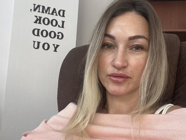 Lilitraya has blonde hair, brown eyes, and is wearing a pink sweater. She's sitting with a neutral expression, showing her pouty lips and slightly freckled face.