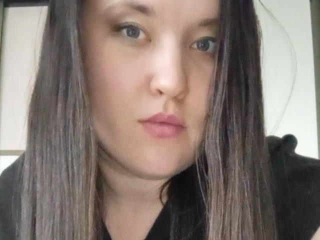 AnnaSova69's face, straight brown hair, pale skin, pink lips, blue eyes, black shirt, slight pout, centered in the image, looking at the camera.