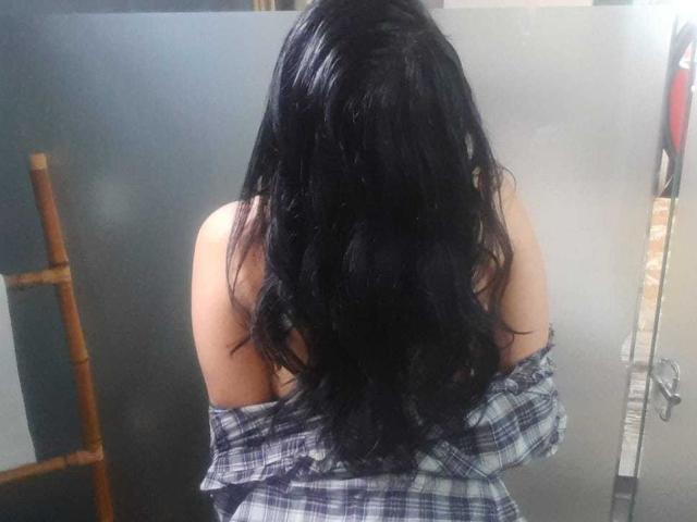 FrancheskaaWaalsh with wet black hair, bare shoulders, and a blue plaid shirt off her back, standing in front of a gray wall. Her back is to the camera.