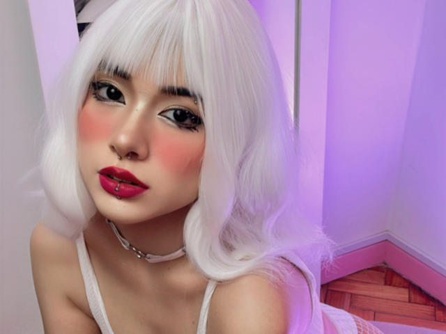 SabriPrettty with white, wavy hair, red lipstick, pierced lower lip, pink blush, black eyeliner, white choker, and red lipstick, looking at the camera, with a cute, sexy expression.