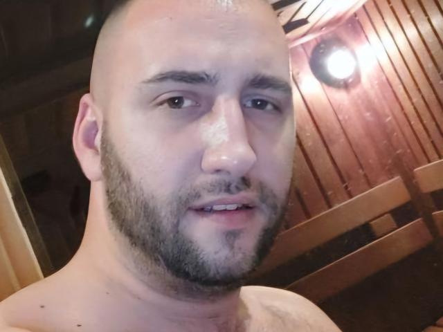 AxelCroftAndFordFairlane has a bald head, light skin, beard, and is shirtless with a slight smile, showing a small tattoo on his right shoulder. He looks relaxed.