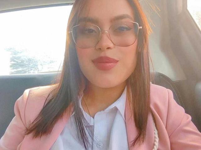 MalejaI has brown hair, wears glasses, and a pink blazer over a white shirt, with pink lipstick, sitting in a car, sunlight in the background.
