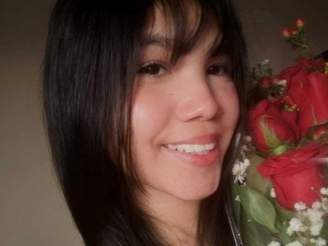 MidnightHarpy's face, smiling with dark straight hair, holding a bouquet of red roses and white baby's breath. She's got cute Asian features and a shiny, happy grin.