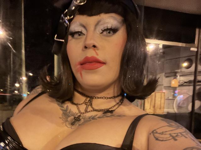 Chili bekommt einen Blowjob im Gesicht, ihr roter Lippenstift ist über ihr Gesicht geschmiert, schwarze Haare, schweres Augen-Make-up und schwarzer BH sichtbar.