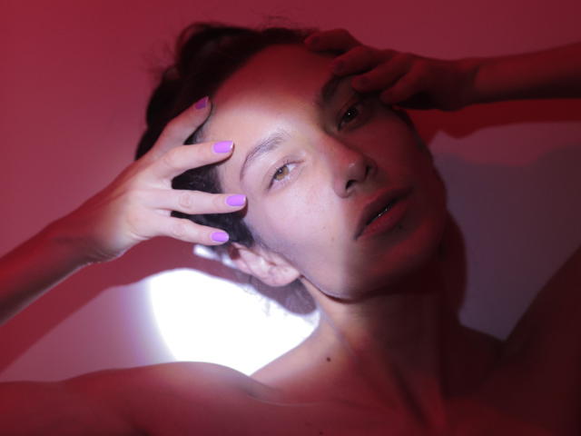 Belicious69 with purple nails, hands in dark hair, red and pink lighting, exposed shoulders, subtle smile, soft skin, and slightly parted lips. She looks sexy and confident.