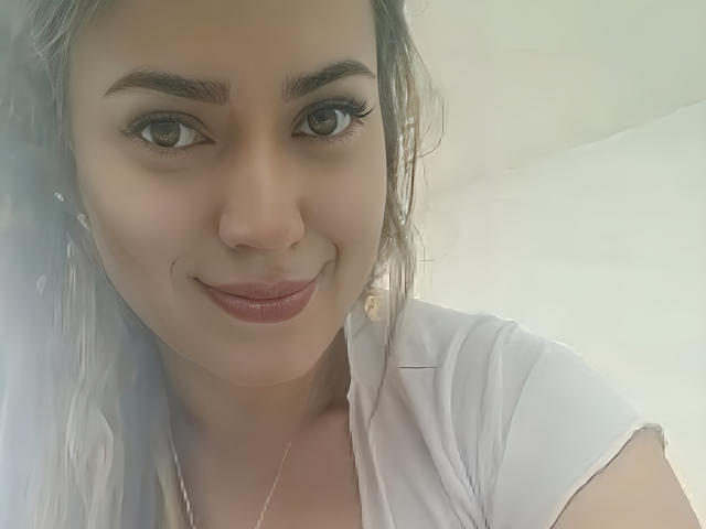 KristenSexy has a cute smile, brown eyes, and subtle makeup. She's wearing a white shirt with a gold necklace, and her gray hair is slightly wavy.