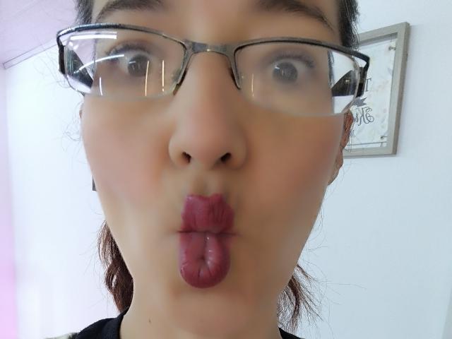 AntonnellaS has puffy, slightly wet, dark pink lips puckered in a kiss. She wears clear glasses with dark frames, and her brown hair is tied back.