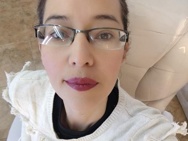AntonnellaS has glasses, pink lipstick, and a white, fringed sweater. Her face is centered, with brown hair pulled back, and she's wearing a black shirt underneath.