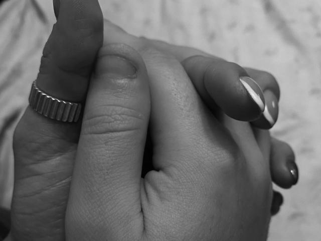 SexLoveHt's hand with a ring on the index finger, holding another hand with long, manicured nails, in black-and-white. The ringed finger is slightly bent.