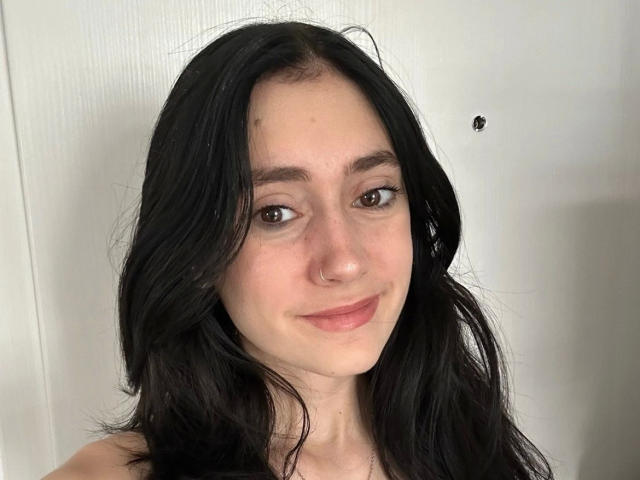 LenaLang-hot has long black hair, brown eyes, a nose ring, and a slight smile. She's a cute chick with fair skin and a small black speck on the wall.