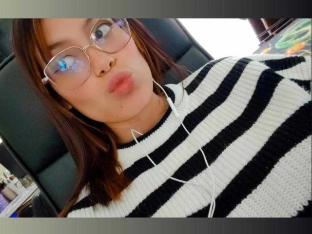 MalejaI with puffy lips, wearing glasses, and a black and white striped sweater, has earbuds in, brown hair, and a slightly chubby face, in a car selfie.