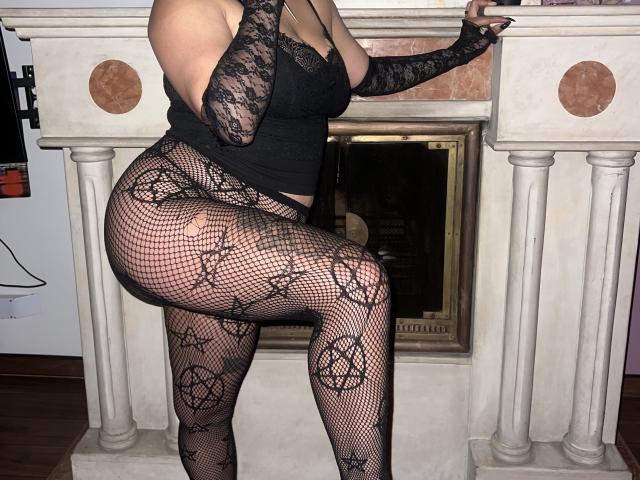 SilenaLee has big tits, wearing black lace gloves, and black fishnet pantyhose with occult patterns, standing in front of a fireplace with her leg raised.