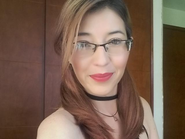 AntonnellaS has glasses, red lipstick, and a black choker, with shoulder-length brown hair, smiling at the camera, showing her tits in a sleeveless top.